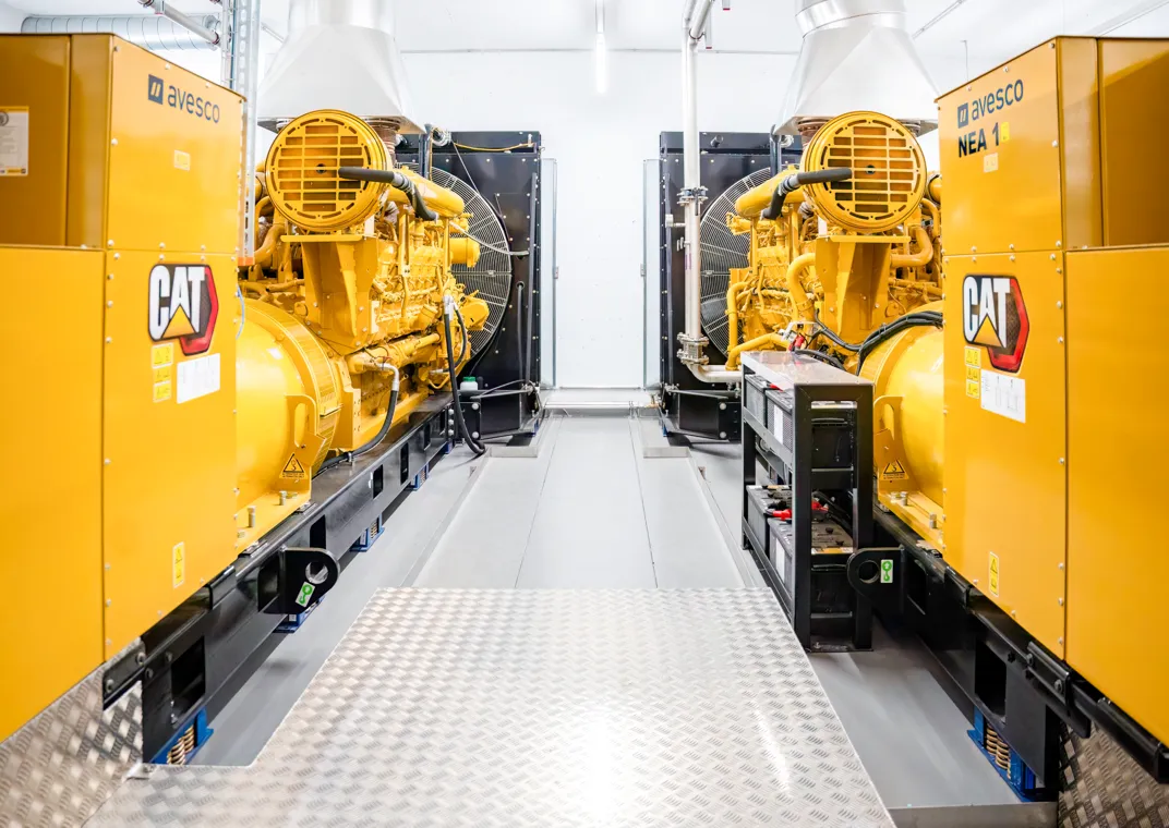Blick in einen hellen Technikraum des Rechenzentrums DATAROCK mit zwei großen, gelben Notstromaggregaten der Marke CAT von Avesco. Die Aggregate stehen sich gegenüber, im Hintergrund sind Lüftungsanlagen und Kabelsysteme sichtbar. Mit diesen Generatoren wird der unterbrechungsfreie Betrieb der Server-Infrastruktur gesichert.