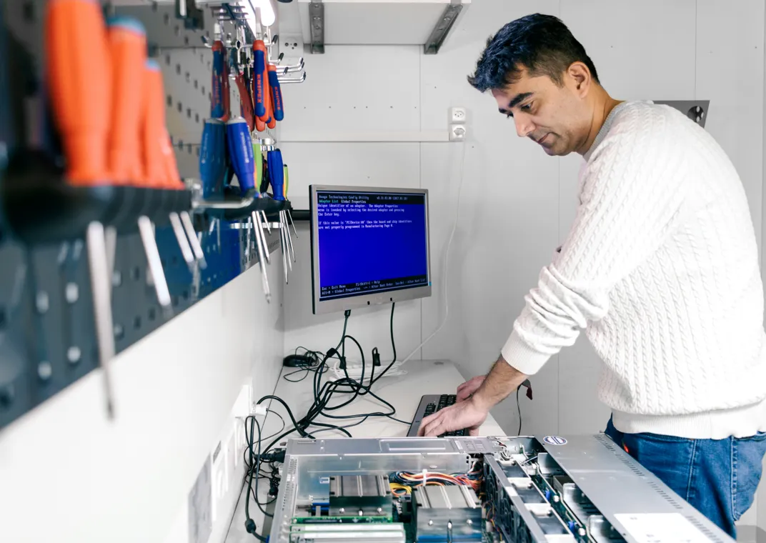 Werkstatt im Datacenter DATAROCK. Amir Dehghani, Head of Datacenter Engineering bei hosttech, prüft die Funktionalität eines Servers. Auf dem weissen Werktisch liegt ein offener Server, welcher mit Kabeln an einen Bildschirm und eine Tastatur angeschlossen ist. Links an der Wand ist ein Lochblech montiert, auf welchem verschiedene Schraubenzieher, Zangen und weitere Werkzeuge befestigt sind.