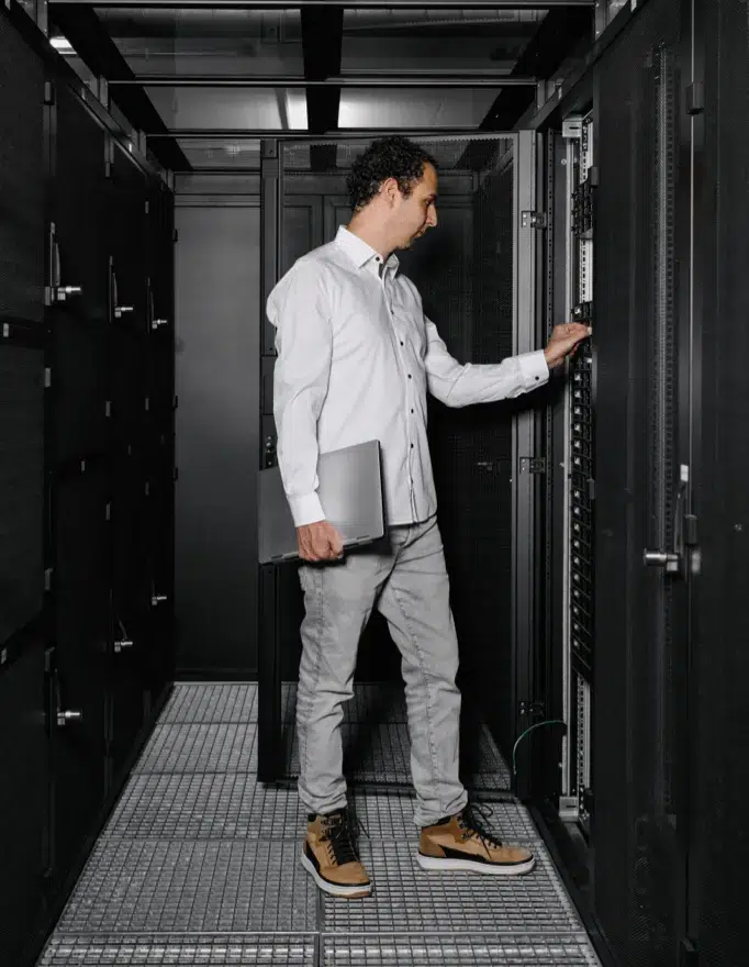 Marius Meuwly, CEO von hosttech, steht vor einem Server-Rack in einem Rechenzentrum von hosttech. Die Tür des Server-Racks ist geöffnet und Marius schiebt mit der linken Hand gerade eine Hardware-Komponente ein. Rechts hält er ein Notebook.