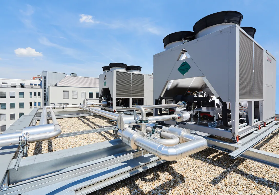 Aufnahme der auf dem Dach installierten Kühlanlage des Rechenzentrums in Wien, in welchem hosttech Server-Infrastruktur betreibt. Zu sehen sind grosse Lüfter und ein Rohrsystem vor blauem Himmel.